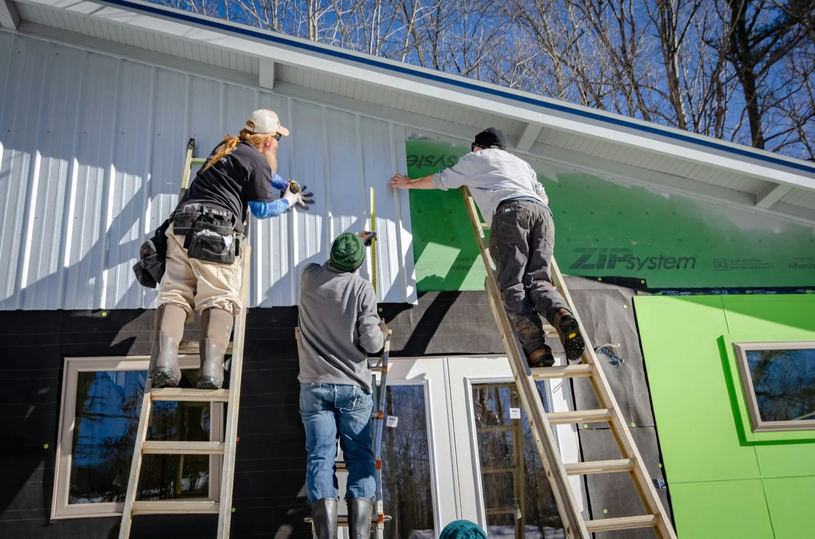 Crew on ladders installing sheathing across a house exterior