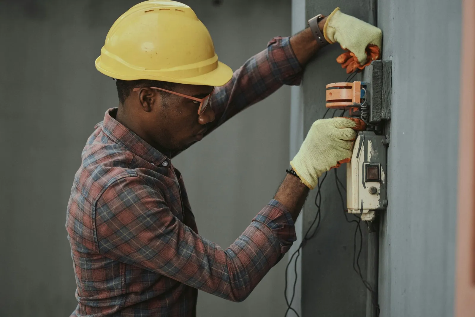 Electrician in a hard hat wiring a panel, hands full mid-job