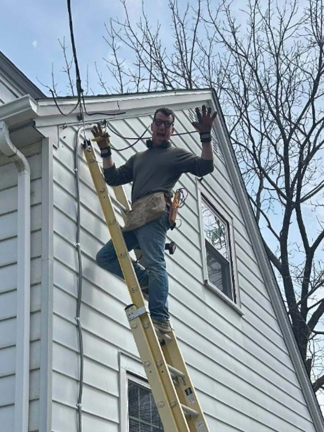Jim Butler throwing his hands up for the camera from the top of an extension ladder on the same house