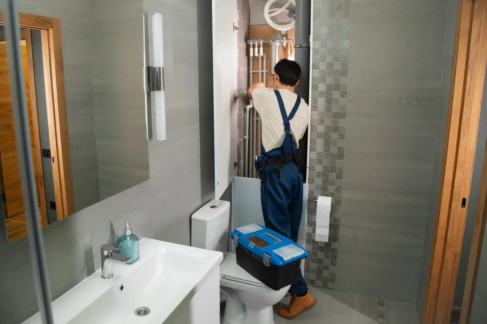 Plumber working behind a bathroom wall panel with an open tool box