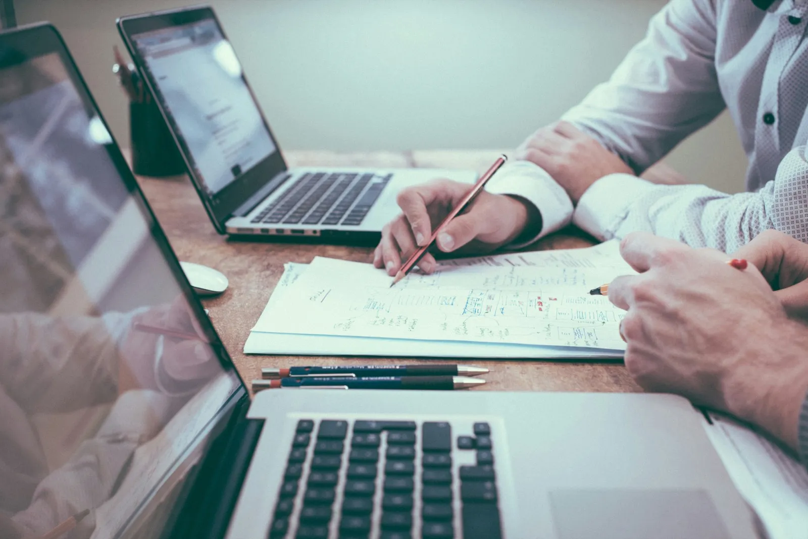 Two people reviewing job numbers across laptops and handwritten notes