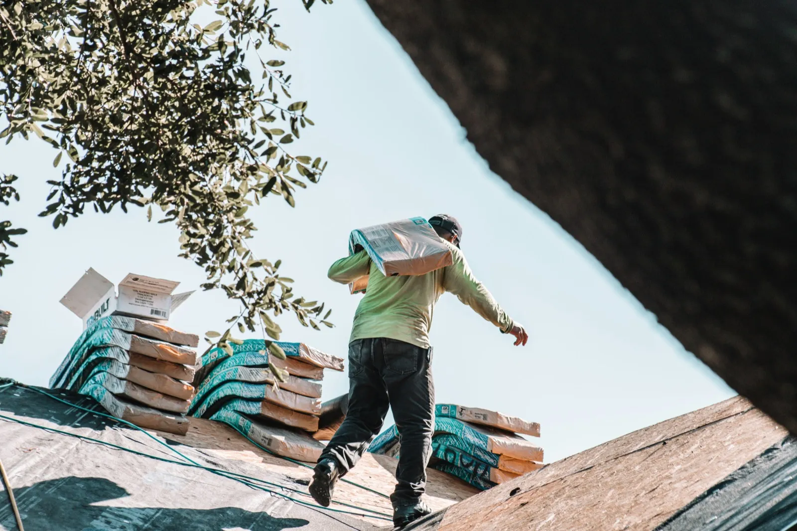 Roofer carrying a bundle of shingles across a roof deck